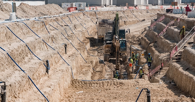 Dewatering excavation site with heavy machinery and construction workers working on underground infrastructure.