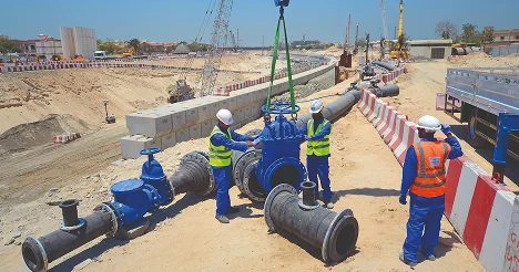 Heavy construction workers installing large pipes at an industrial site, focusing on pipeline installation, construction safety, and infrastructure development in Middle East projects.